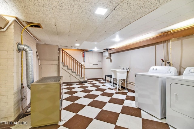 finished below grade area featuring a drop ceiling, washing machine and clothes dryer, tile patterned floors, stairs, and a sink