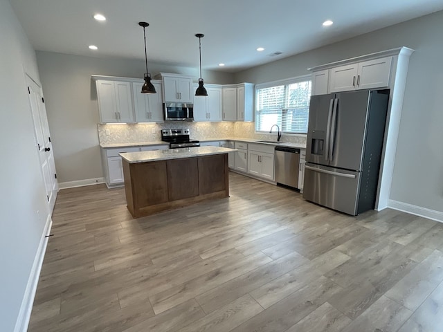 kitchen with stainless steel appliances, a sink, decorative light fixtures, and white cabinets