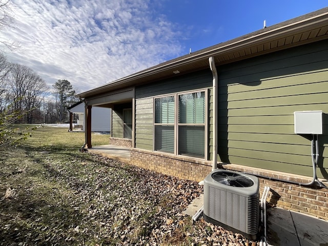 view of home's exterior with brick siding, a lawn, cooling unit, and a patio