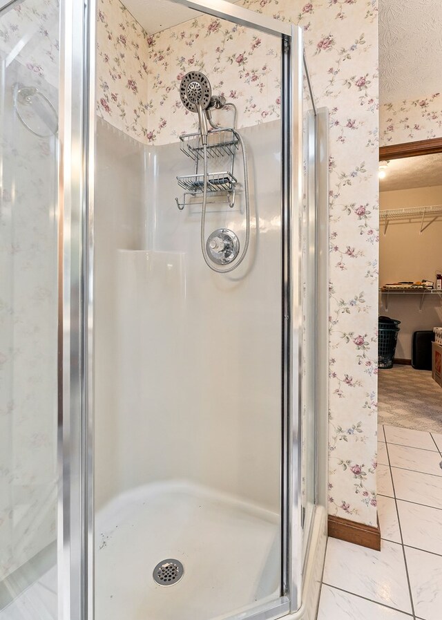 bathroom featuring a spacious closet, a shower stall, and wallpapered walls