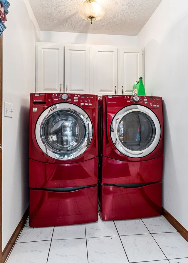 laundry area with marble finish floor, cabinet space, a textured ceiling, washer and dryer, and baseboards