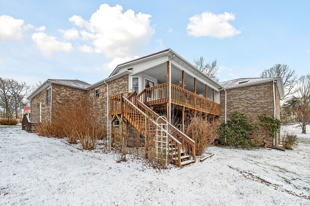 snow covered house featuring a deck, brick siding, and stairway