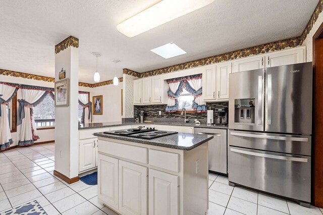 kitchen with stainless steel appliances, a sink, a kitchen island, white cabinets, and dark countertops