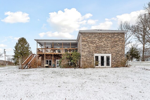 snow covered rear of property with french doors, brick siding, ceiling fan, a deck, and stairs