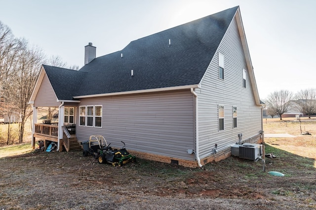 rear view of property with a shingled roof, cooling unit, a chimney, and crawl space