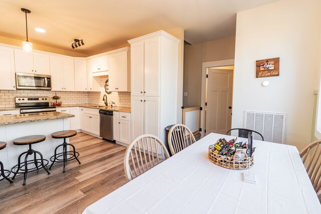 kitchen with visible vents, light wood-style flooring, appliances with stainless steel finishes, a kitchen bar, and tasteful backsplash