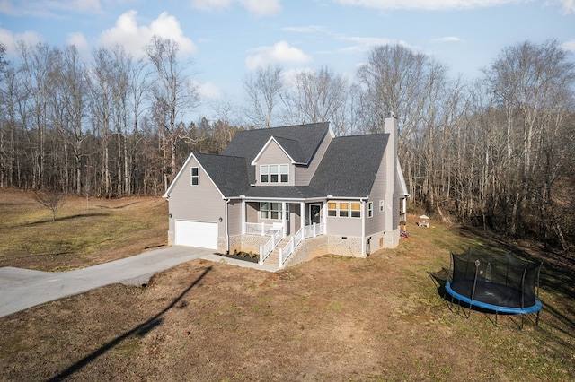 traditional-style house featuring a front yard, an attached garage, covered porch, concrete driveway, and a trampoline