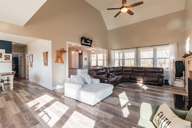 living room featuring baseboards, high vaulted ceiling, wood finished floors, and a ceiling fan