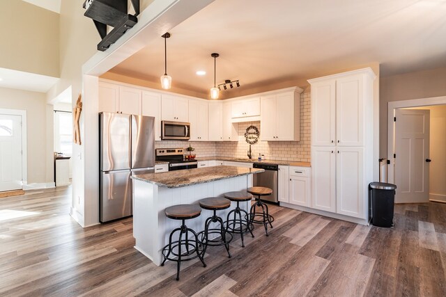 kitchen with a kitchen bar, a center island, stainless steel appliances, white cabinets, and decorative backsplash