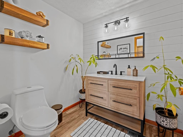 bathroom featuring a textured ceiling, toilet, wooden walls, wood finished floors, and vanity