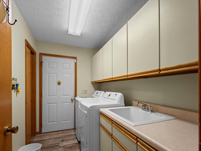 washroom with cabinet space, wood finished floors, washing machine and clothes dryer, a textured ceiling, and a sink