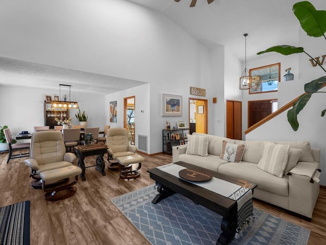 living room with high vaulted ceiling, visible vents, wood finished floors, and ceiling fan with notable chandelier