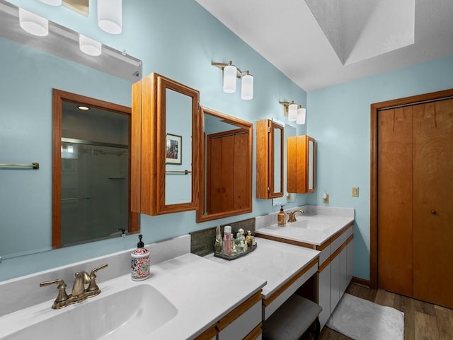 bathroom with double vanity, a shower with shower door, a sink, and wood finished floors