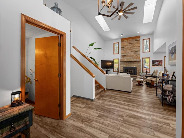 living room with high vaulted ceiling, a stone fireplace, a skylight, wood finished floors, and stairway