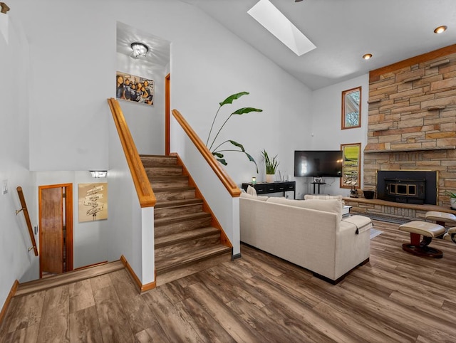 living area featuring a skylight, a fireplace, wood finished floors, high vaulted ceiling, and stairs