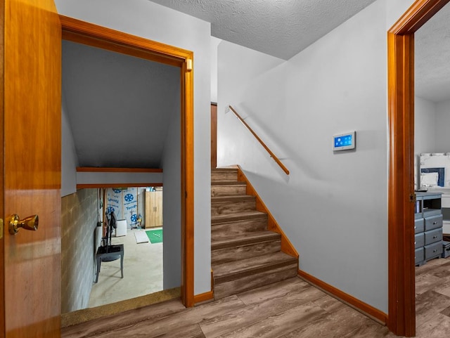 staircase with a textured ceiling, wood finished floors, and baseboards