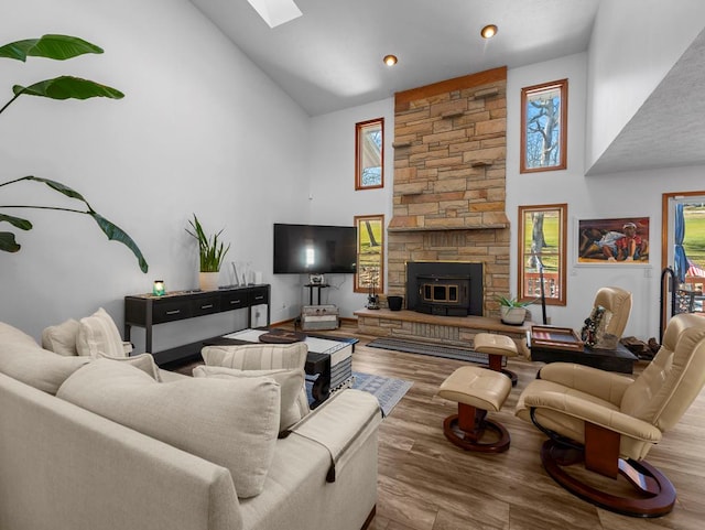 living area featuring a skylight, high vaulted ceiling, a fireplace, and wood finished floors