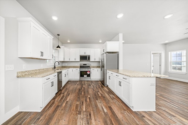 kitchen featuring stainless steel appliances, a sink, white cabinetry, hanging light fixtures, and light stone countertops