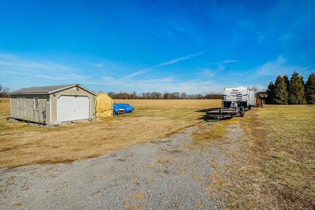 view of yard featuring a rural view, a detached garage, and an outdoor structure