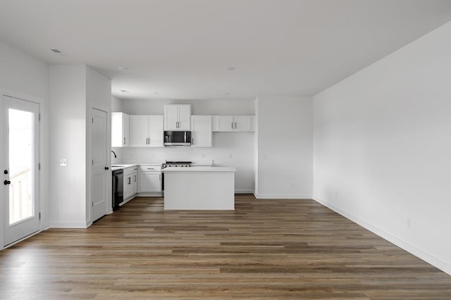 kitchen with a kitchen island, wood finished floors, white cabinets, black dishwasher, and stainless steel microwave