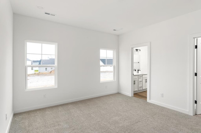 unfurnished bedroom with visible vents, baseboards, light colored carpet, ensuite bathroom, and a sink