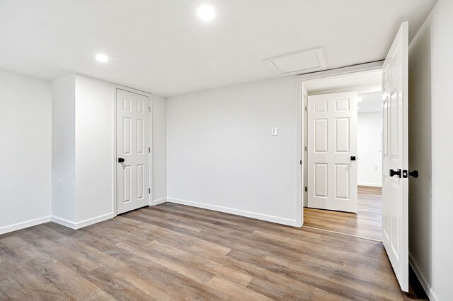 unfurnished room with recessed lighting, wood finished floors, attic access, and baseboards