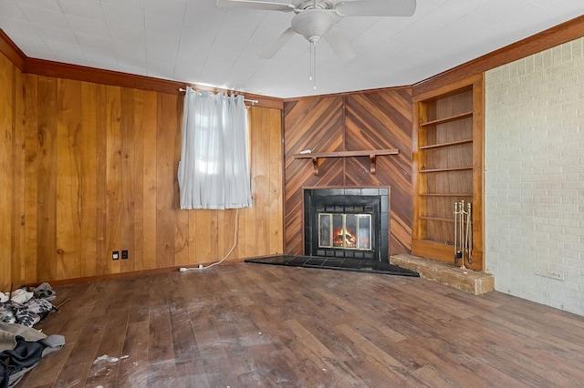 unfurnished living room featuring a glass covered fireplace, built in shelves, wooden walls, and wood-type flooring