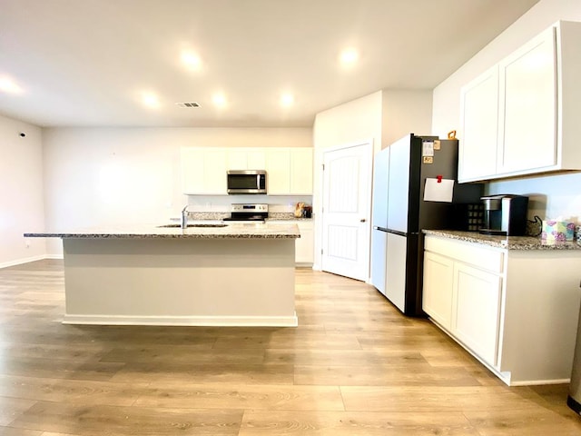 kitchen with stainless steel appliances, a sink, white cabinetry, light stone countertops, and light wood finished floors