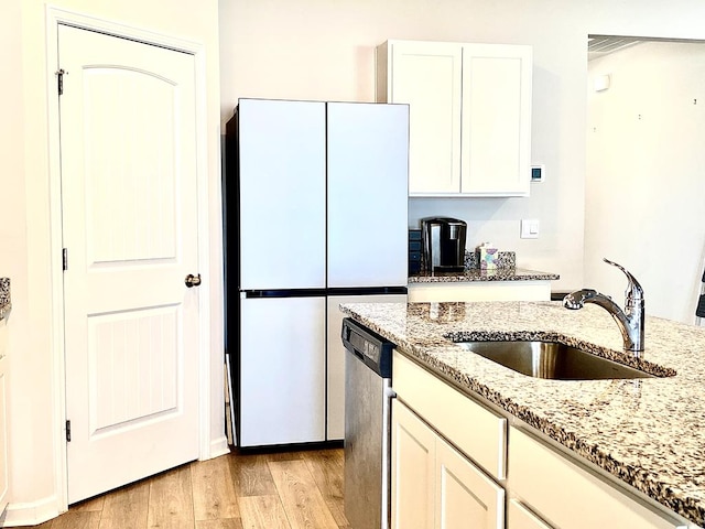 kitchen with light wood-style flooring, a sink, stainless steel dishwasher, freestanding refrigerator, and light stone countertops