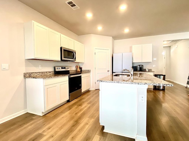 kitchen featuring a sink, visible vents, appliances with stainless steel finishes, light wood-type flooring, and light stone countertops