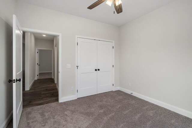 unfurnished bedroom with baseboards, dark carpet, ceiling fan, and a closet