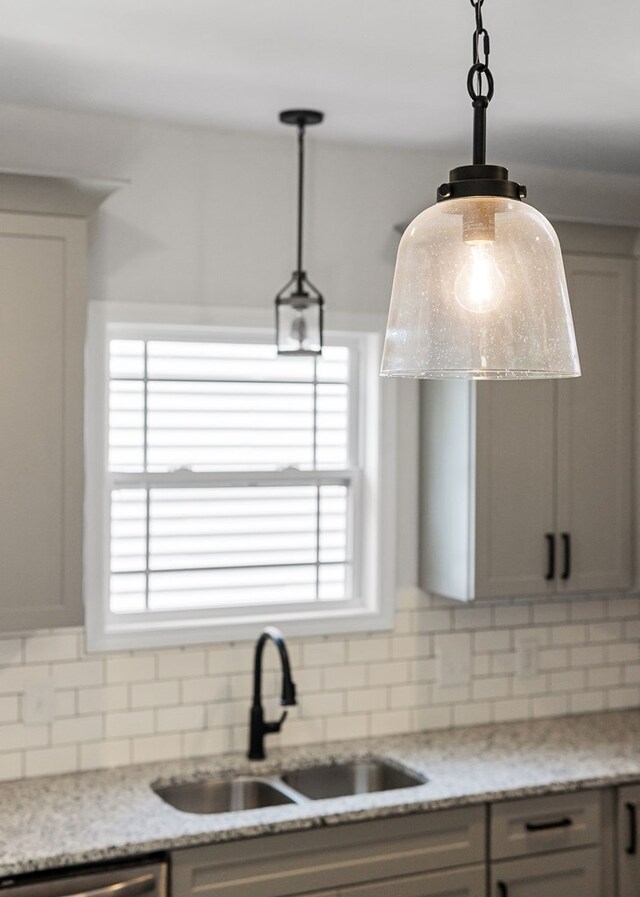 kitchen featuring decorative light fixtures, a sink, backsplash, and light stone countertops