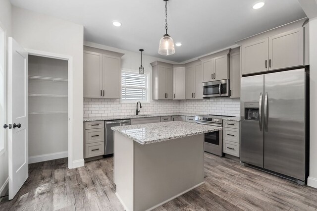 kitchen featuring stainless steel appliances, hanging light fixtures, gray cabinetry, a kitchen island, and a sink