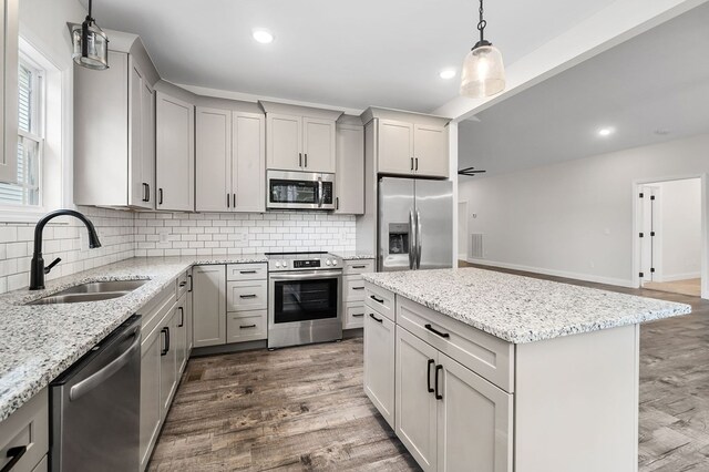 kitchen with light stone countertops, a kitchen island, appliances with stainless steel finishes, and a sink