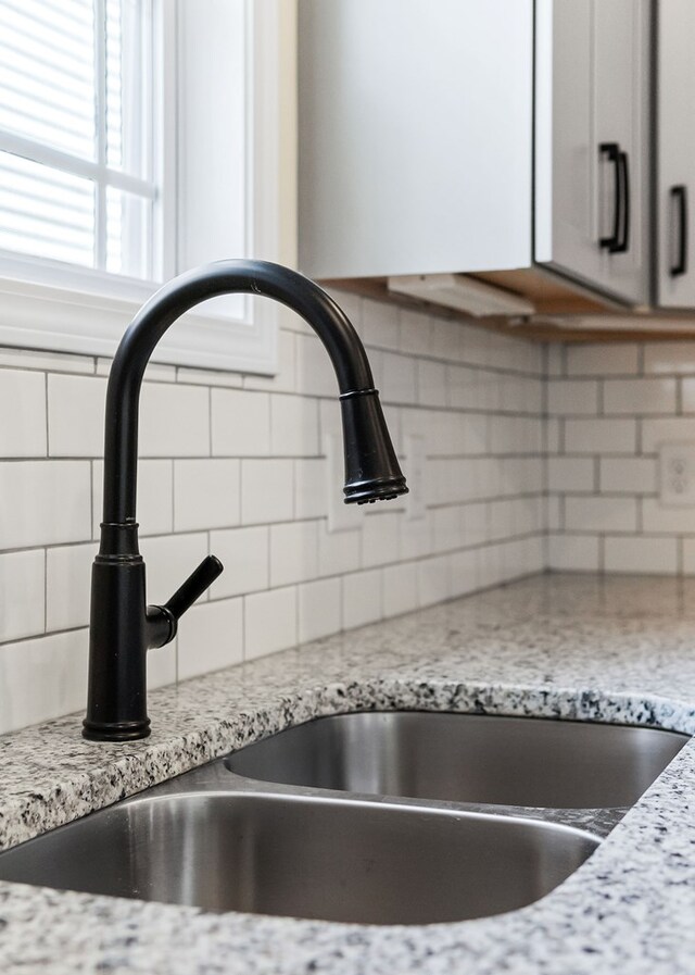 room details featuring light stone counters, backsplash, a sink, and white cabinets