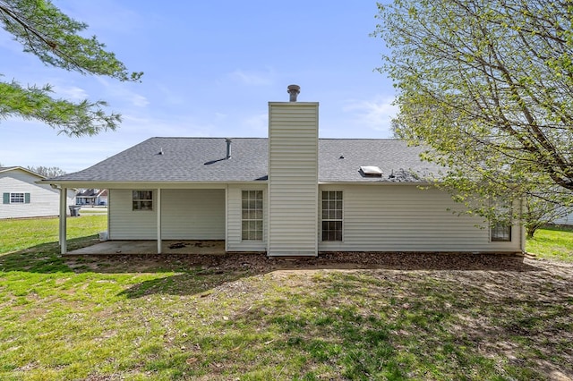 back of property with a lawn, a chimney, a patio area, and roof with shingles
