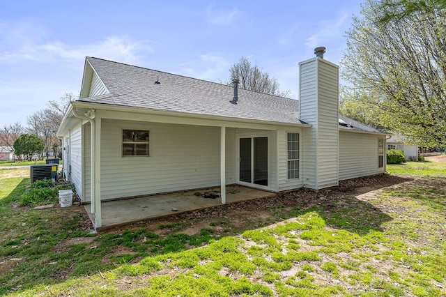 back of house featuring a chimney, central AC, a shingled roof, and a patio area