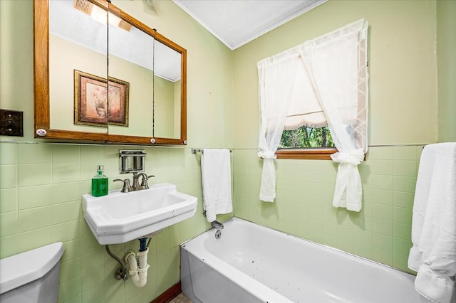 full bath with a garden tub, toilet, a wainscoted wall, a sink, and tile walls