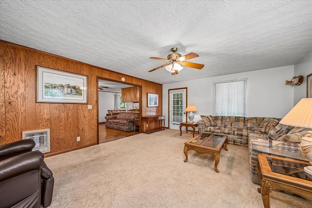 carpeted living room featuring heating unit, a textured ceiling, wooden walls, and a ceiling fan