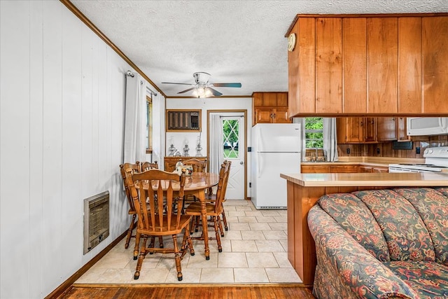 kitchen featuring a peninsula, white appliances, light countertops, brown cabinets, and heating unit