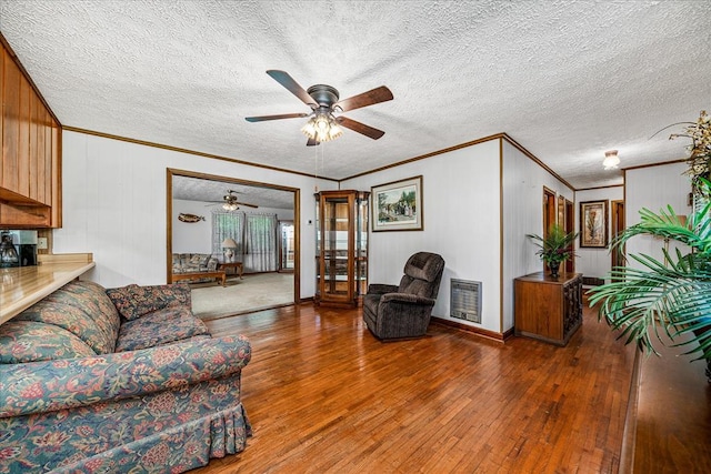 living room featuring heating unit, a textured ceiling, ornamental molding, and wood finished floors