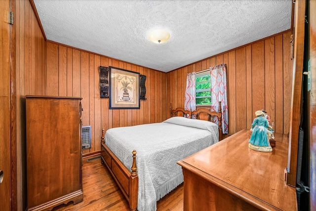 bedroom featuring wooden walls, a textured ceiling, and wood finished floors