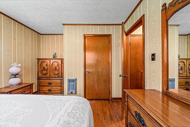 bedroom featuring ornamental molding, light wood-type flooring, a textured ceiling, and heating unit