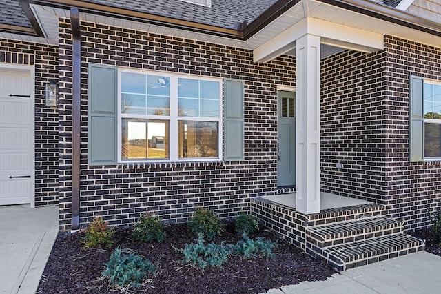 property entrance featuring brick siding, roof with shingles, and an attached garage