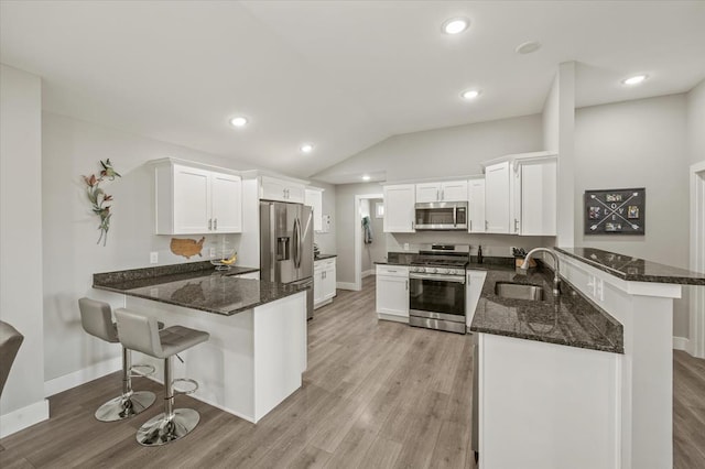kitchen featuring a sink, dark stone countertops, appliances with stainless steel finishes, and a peninsula