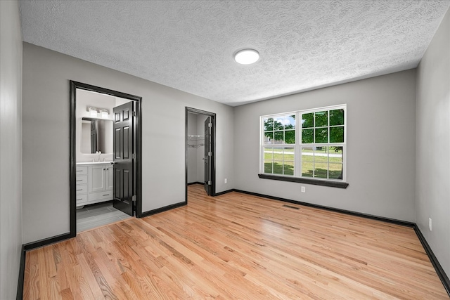 unfurnished bedroom featuring a walk in closet, a closet, light wood-style flooring, ensuite bath, and baseboards