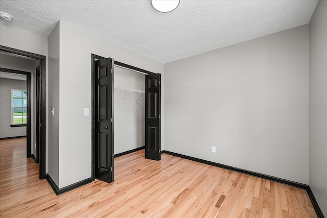 unfurnished bedroom featuring light wood-style floors, a closet, a textured ceiling, and baseboards