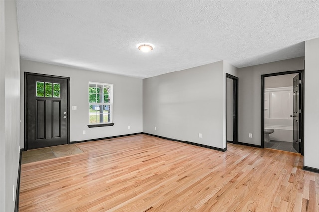 entryway with light wood finished floors, baseboards, and a textured ceiling