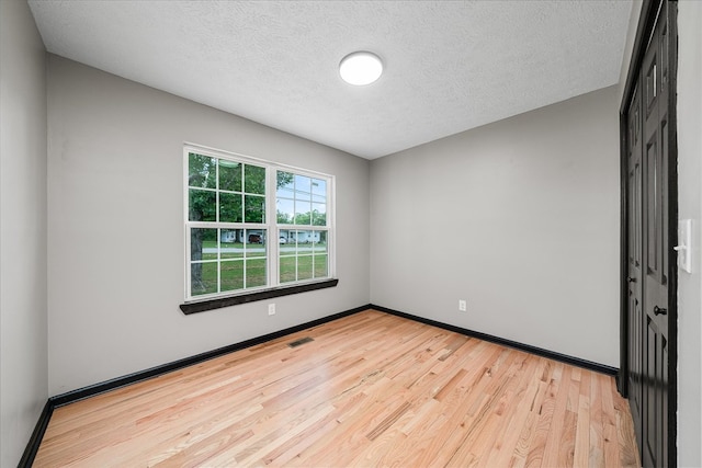 unfurnished room featuring baseboards, a textured ceiling, visible vents, and light wood-style floors