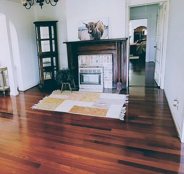 interior space featuring arched walkways, a notable chandelier, a fireplace, heating unit, and dark wood finished floors